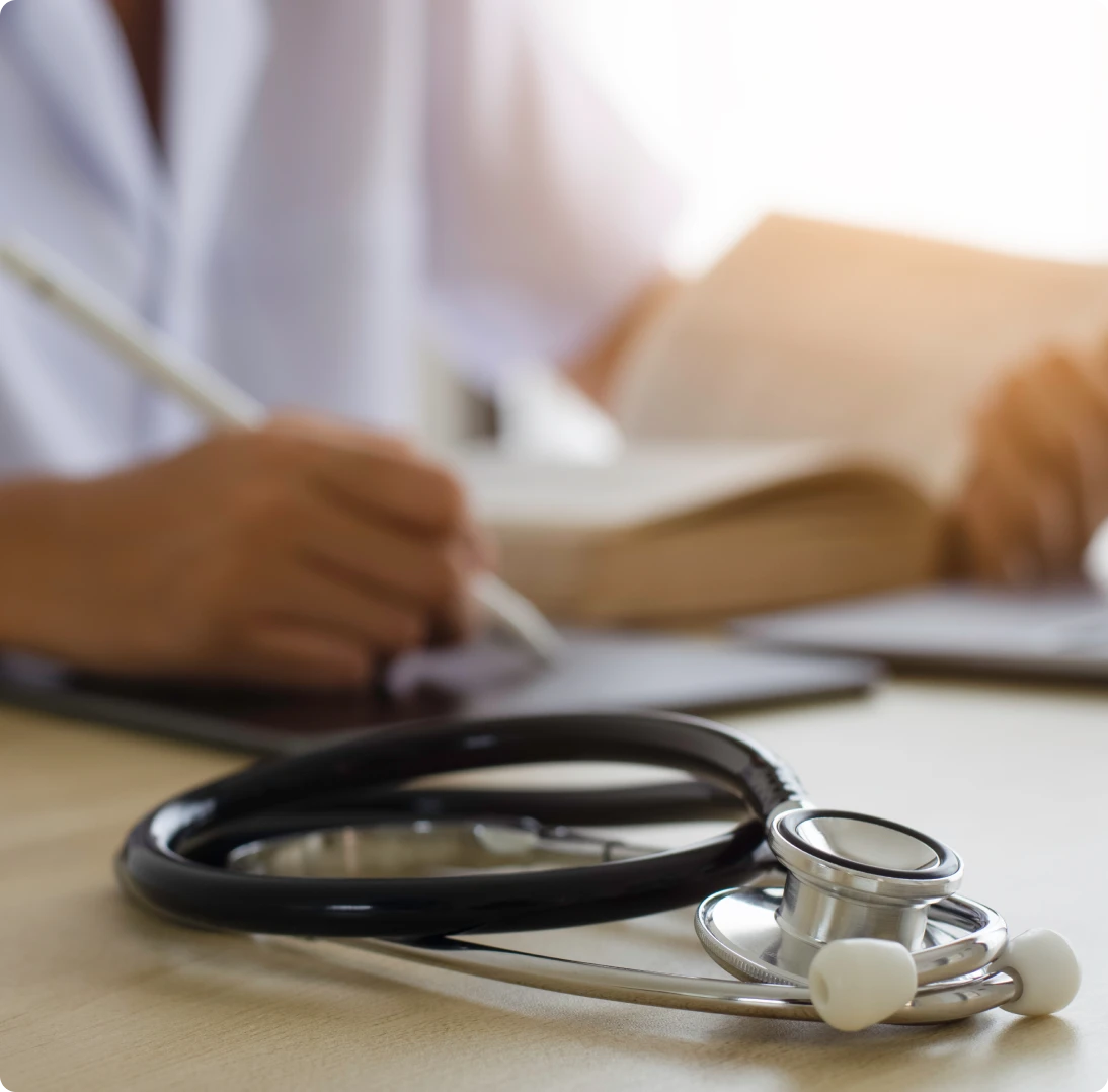 Doctor writing with stethoscope on desk