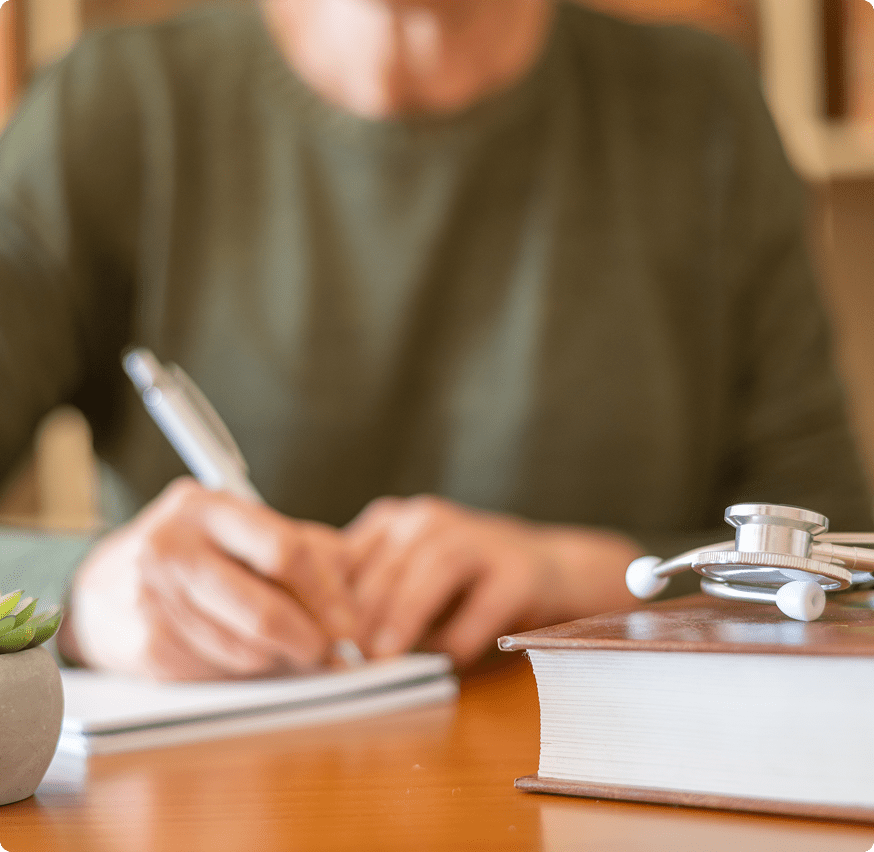 Hands writing beside a plant and book